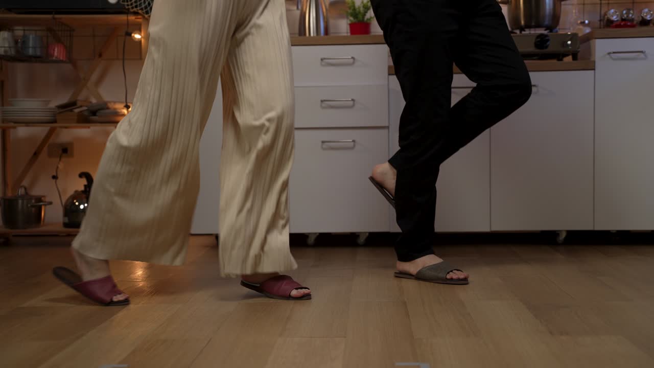 cropped shot of a couple’s feet in household slippers doing lively partner dance on wood floor at home