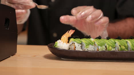 chef poniendo huevas encima de rollos de sushi de camarones tempura en un plato - toma panorámica de cerca