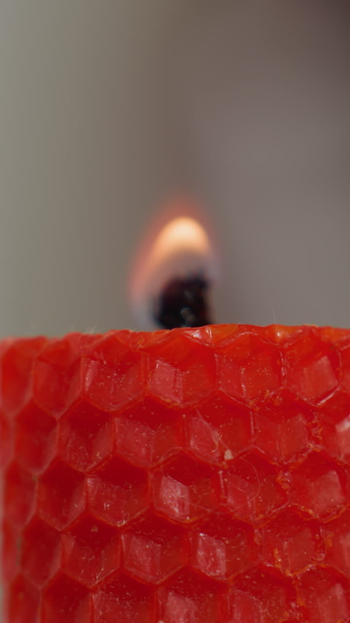 Primissimo piano di una candela rossa accesa con un fiammifero da una persona con unghie curate, la luce soffusa della fiamma esalta l'atmosfera calda e accogliente