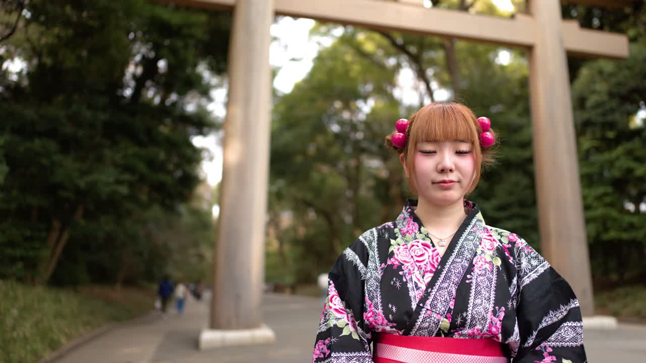 Una donna in abito tradizionale giapponese si trova davanti a un portale torii in legno a Tokyo.