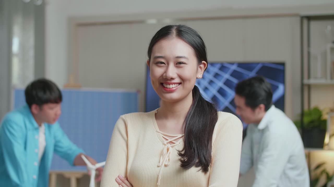 동료들이 사무실에서 태양전지 작업에 대해 논의하는 동안 미소 짓는 아시아 여성 엔지니어가 카메라에 팔을 고 있습니다.