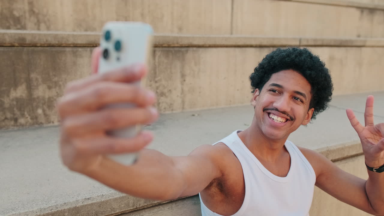 Giovane uomo che si scatta un selfie e saluta sui gradini di cemento