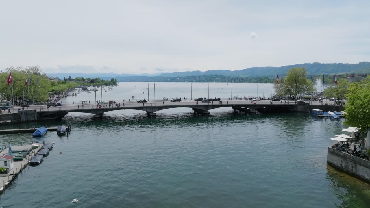 Slow reversing drone shot showing the main bridge of the city, pedestrians, transport and Lake Zurich