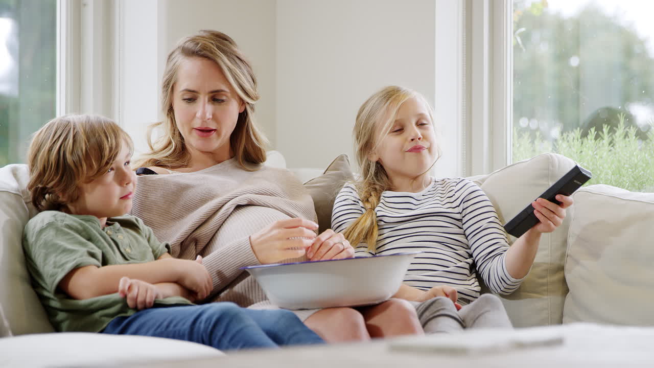 집에서 소파에 앉아 웃고 팝콘과 함께 tv를 보는 아이들과 함께 임신 한 어머니