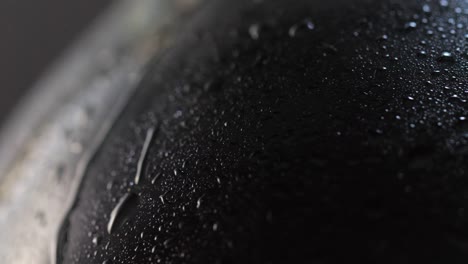 Macro-detail-shot:-a-dark-wine-bottle-on-a-rotating-surface,-full-of-tiny-water-drops,-with-a-big-one-coming-down-the-surface