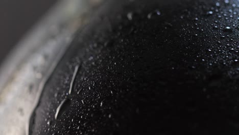 foto de detalle macro: una botella de vino oscura sobre una superficie giratoria, llena de pequeñas gotas de agua, con una grande bajando por la superficie