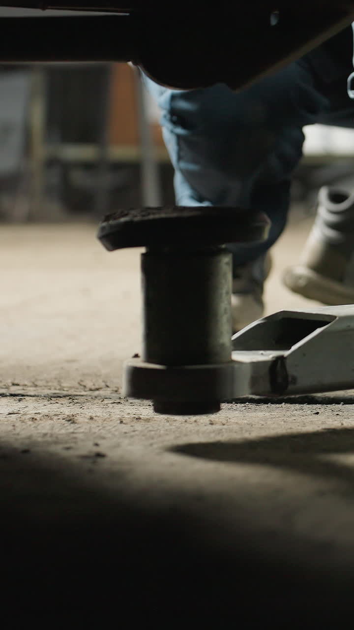 Lower angle view captures an engineer's hairy hand placing a car lift under a vehicle in an auto repair shop, emphasizing the precision of the task