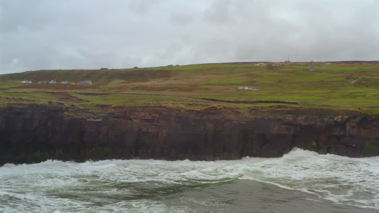 Dynamic aerial pan over the Cliffs of Moher at Doolin with waves crashing on dark rocks