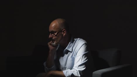 depressed mature man struggling with mental health sitting in darkness on sofa with low key lighting 3