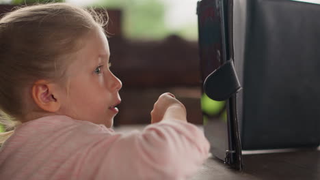 Little-girl-in-pink-jacket-presses-keys-on-tablet-screen