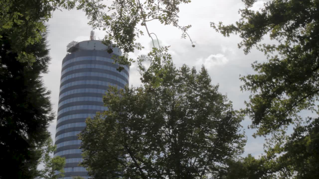 Modern skyscraper peeking through lush green trees on a cloudy day, blending urban architecture with nature