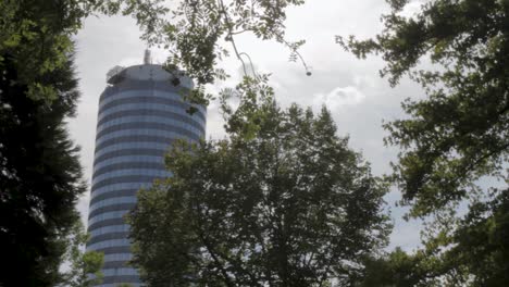 modern skyscraper peeking through lush green trees on a cloudy day, blending urban architecture with nature