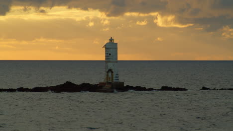 einsamer leuchtturm auf einer winzigen insel vor sonnenbeschienenem horizont zur goldenen stunde