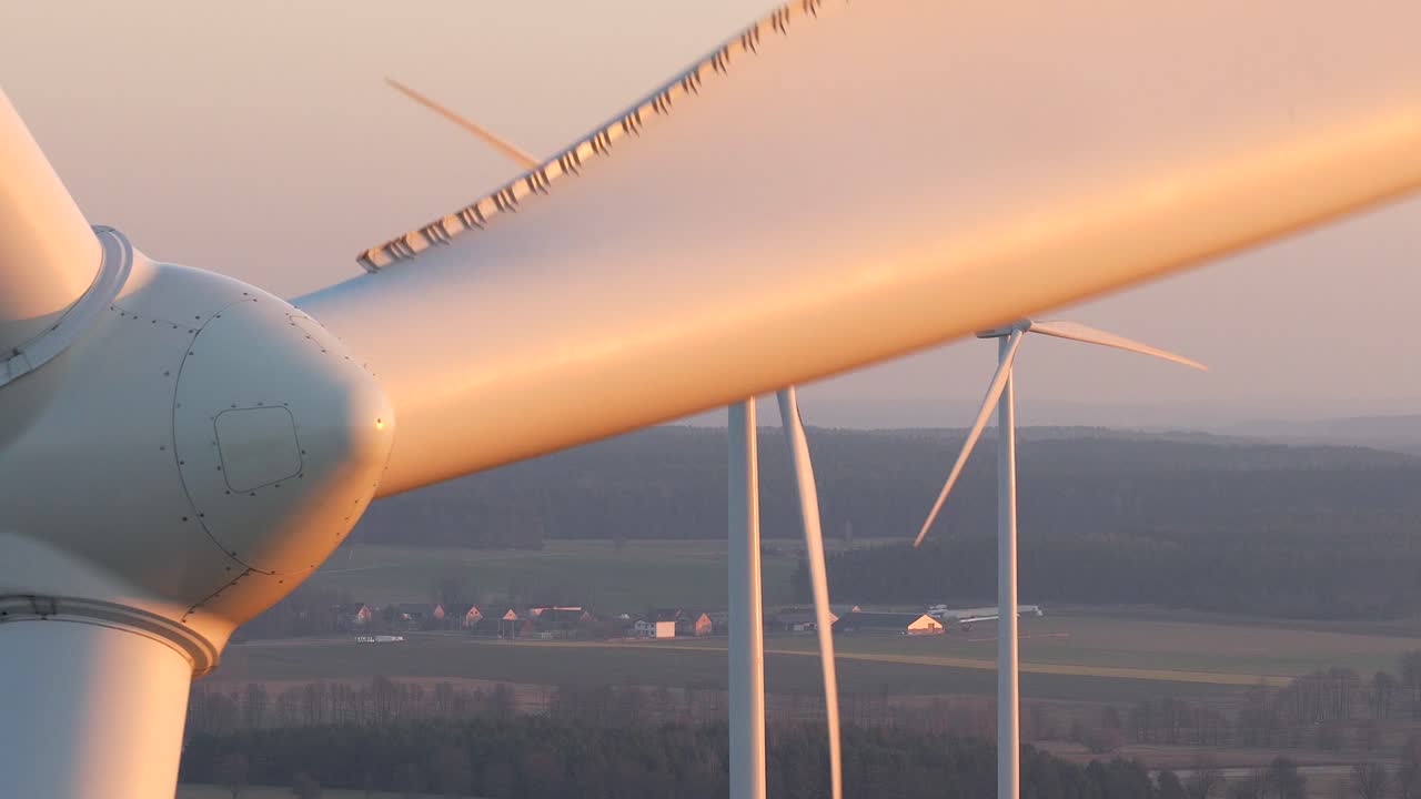 Vista aérea de cerca mostrando las palas de un aerogenerador girando contra un cielo al atardecer. Producción de energía limpia y renovable en un parque eólico.