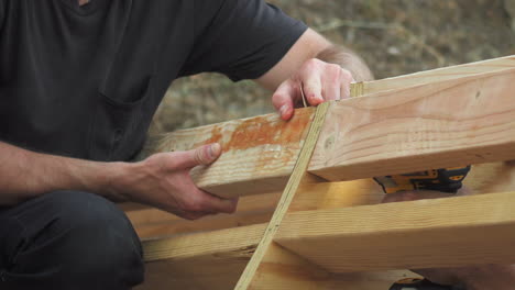 primer plano de las manos del hombre sosteniendo un tablón de madera mientras la persona perfora el tornillo, rampa de patineta casera de bricolaje en el patio trasero