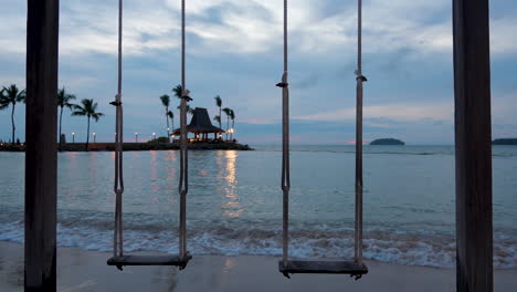 wooden swing on a tropical remote dream honeymoon beach at the seaside with small islands in background at sunset, dramatic courful sky