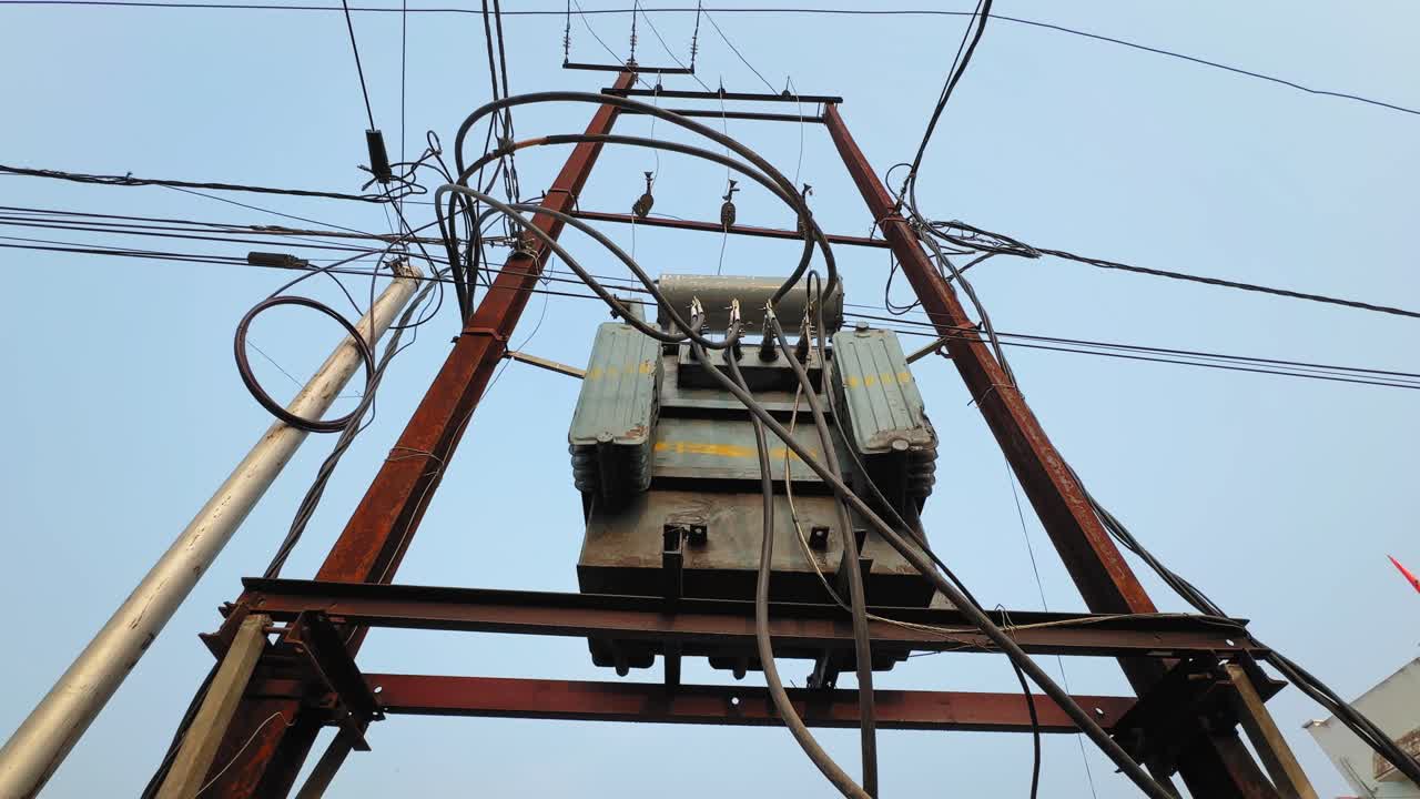 Tracking shot of pole-mounted distribution transformer on H-type structure with cables and insulators, stepping down high-voltage power against open sky background. scene