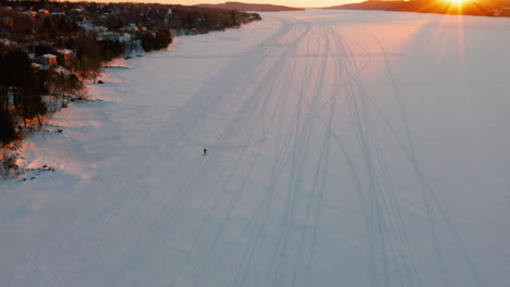 Puesta-De-Sol-Escénica-Aérea-De-Un-Lago-Congelado-Como-Una-Persona-Con-Raquetas-De-Nieve-A-Lo-Largo-Del-Hielo-Y-La-Nieve