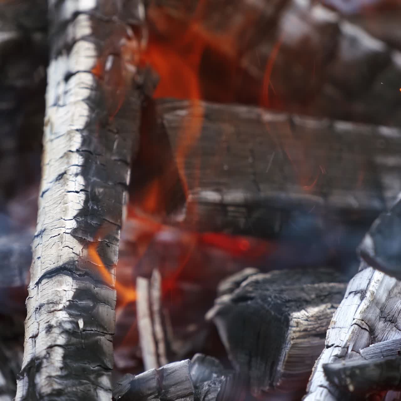 Wooden embers in flame. Smoldered black logs burning out in fire. Background of charcoals in slight orange flame. Close-up.
