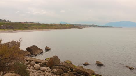 sicilian coastline in italy with rocky outcrops and waves splashing with cloudy sky and mount etna in distance. wide shot