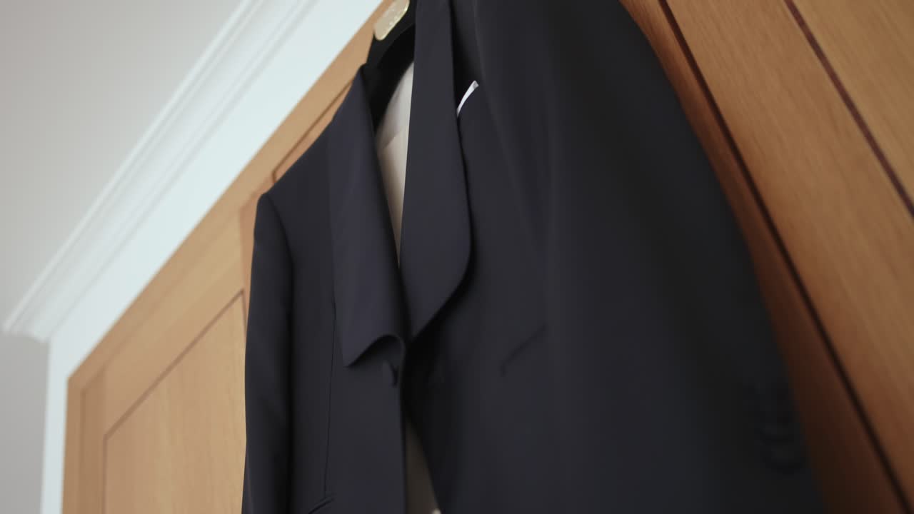 black wedding suit jacket hanging neatly on wooden door ready for groom to dress