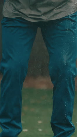 Male-golfer-snaps-water-droplets-off-waterproof-blue-pants-in-pouring-rain-in-slow-motion