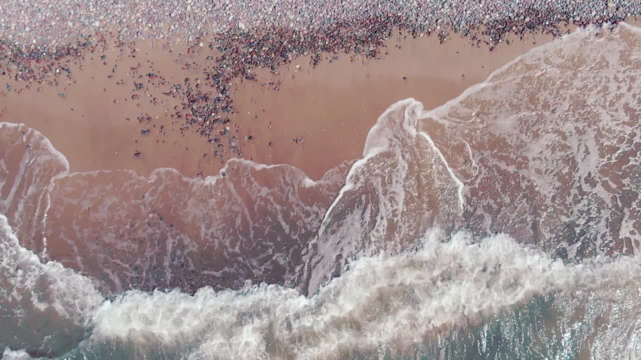 Ocean waves hitting sandy beach with small pebbles, aerial top down view