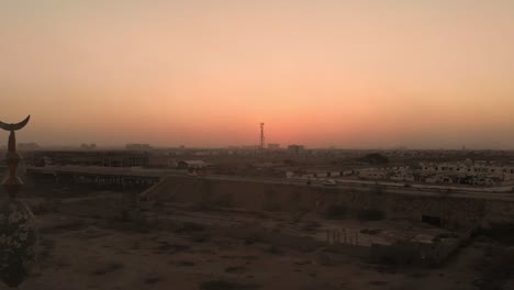 Vista-Aérea-Del-Minarete-De-La-Mezquita-Cerca-De-La-Autopista-En-Karachi-Contra-El-Cielo-Amarillo-Anaranjado-Del-Atardecer