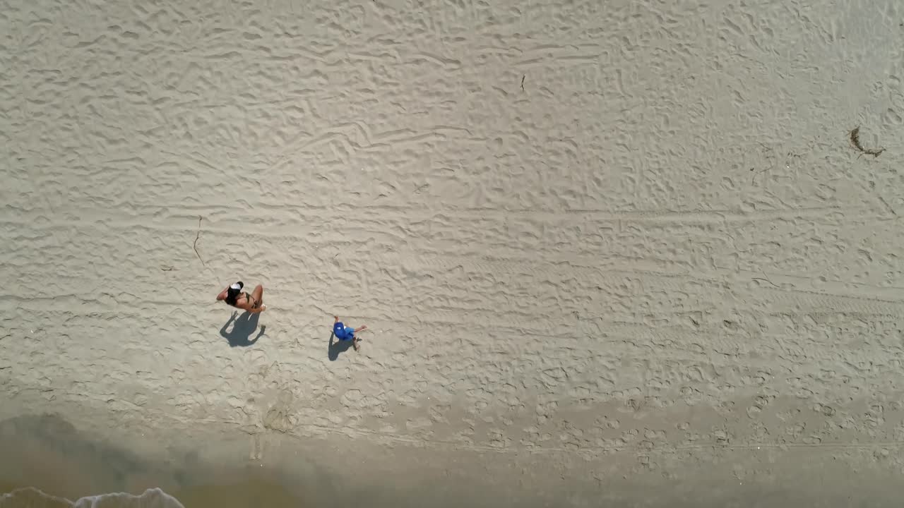 Donna con bambino piccolo esce dal mare e attraversa la spiaggia.