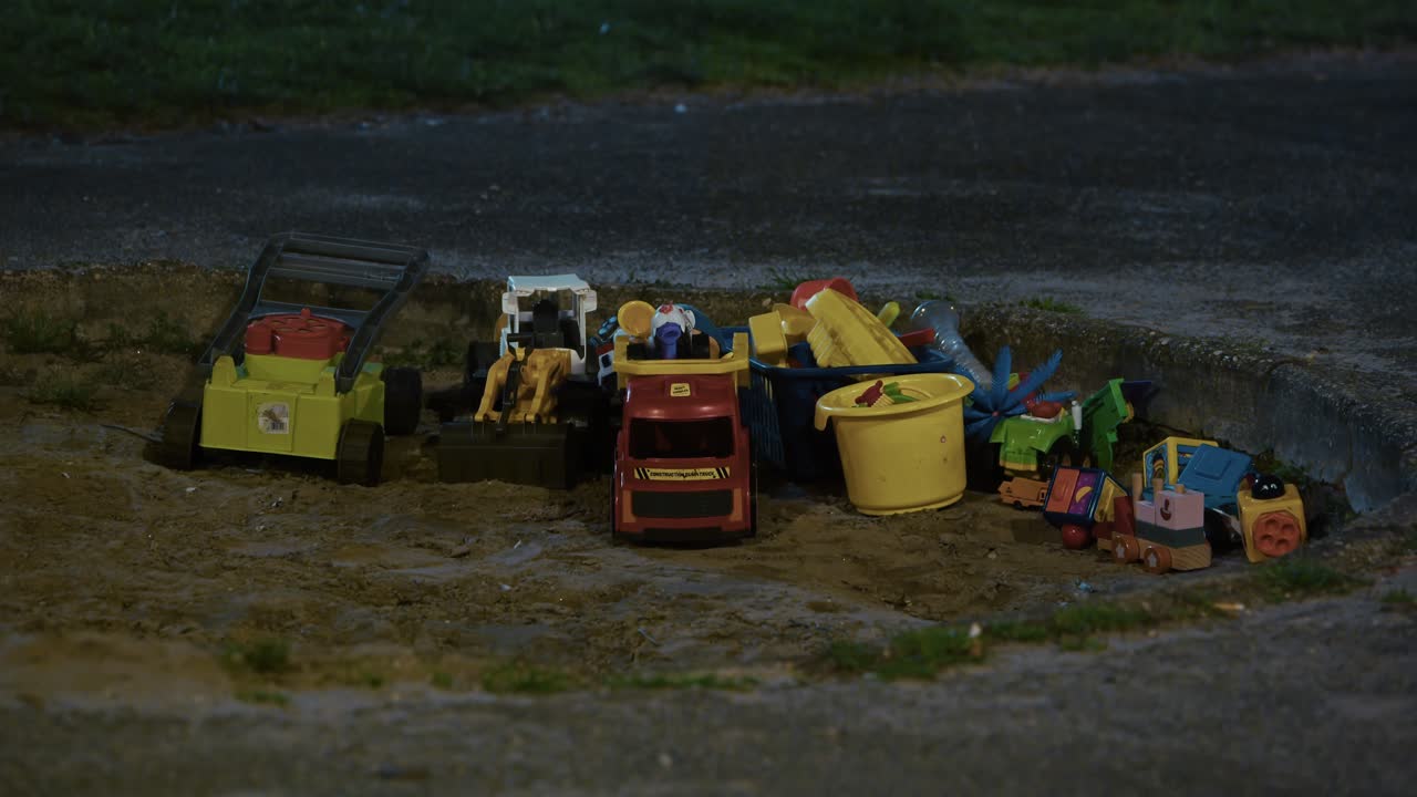 Plastic toys scattered in a sandbox under dim night lighting