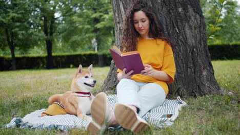 woman reading a book in a park with her dog