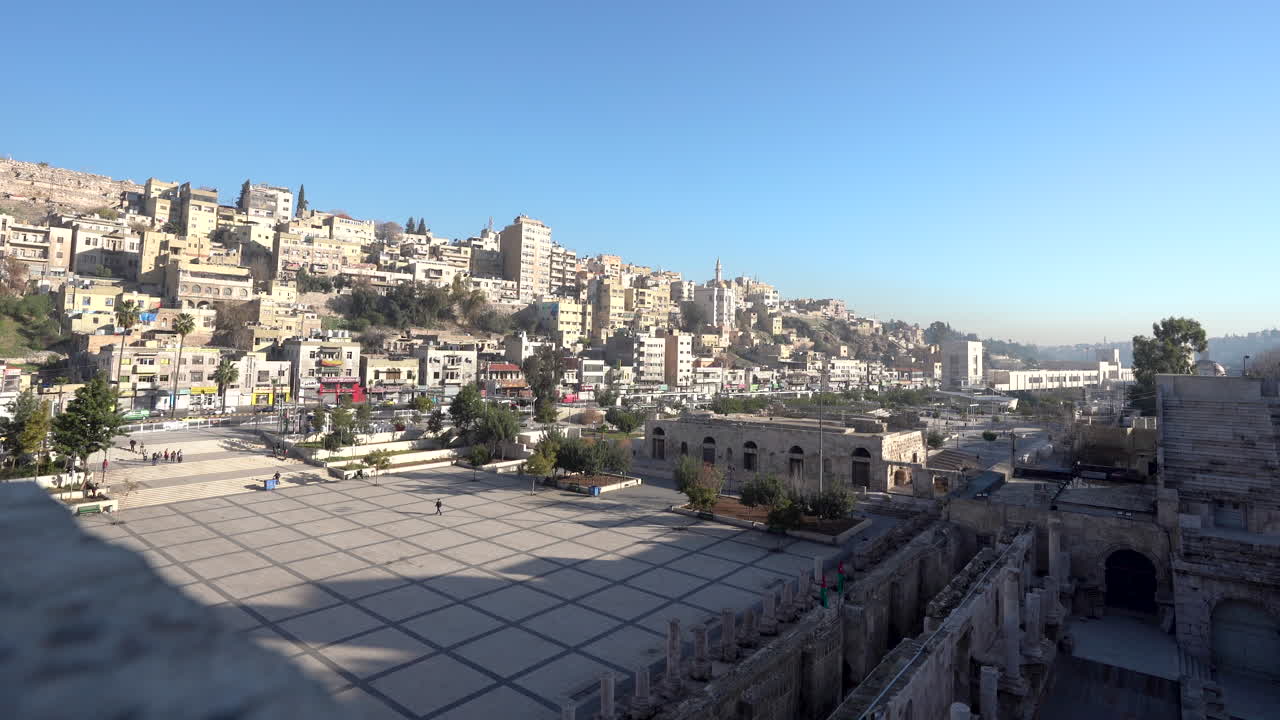 toma fija del panorama de la ciudad de amman con casas en la colina y ruinas en el marco