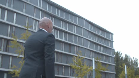 bald businessman in formal suit walking near office building