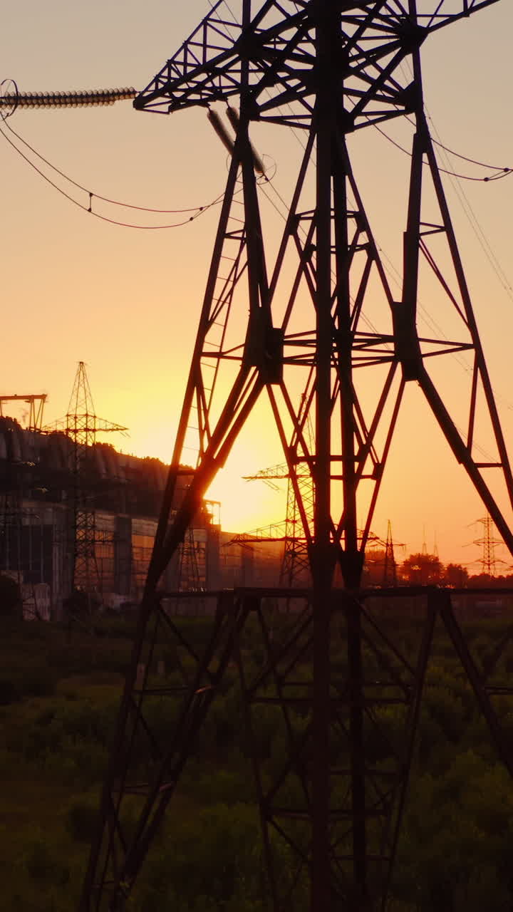 Tall voltage tower. Distribution and supply electricity at sunset. Power electric station with transmission lines against the orange sun. Camera rising up. Vertical video