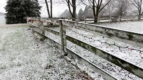 wooden farm fence decorated with christmas lights during heavy snowfall