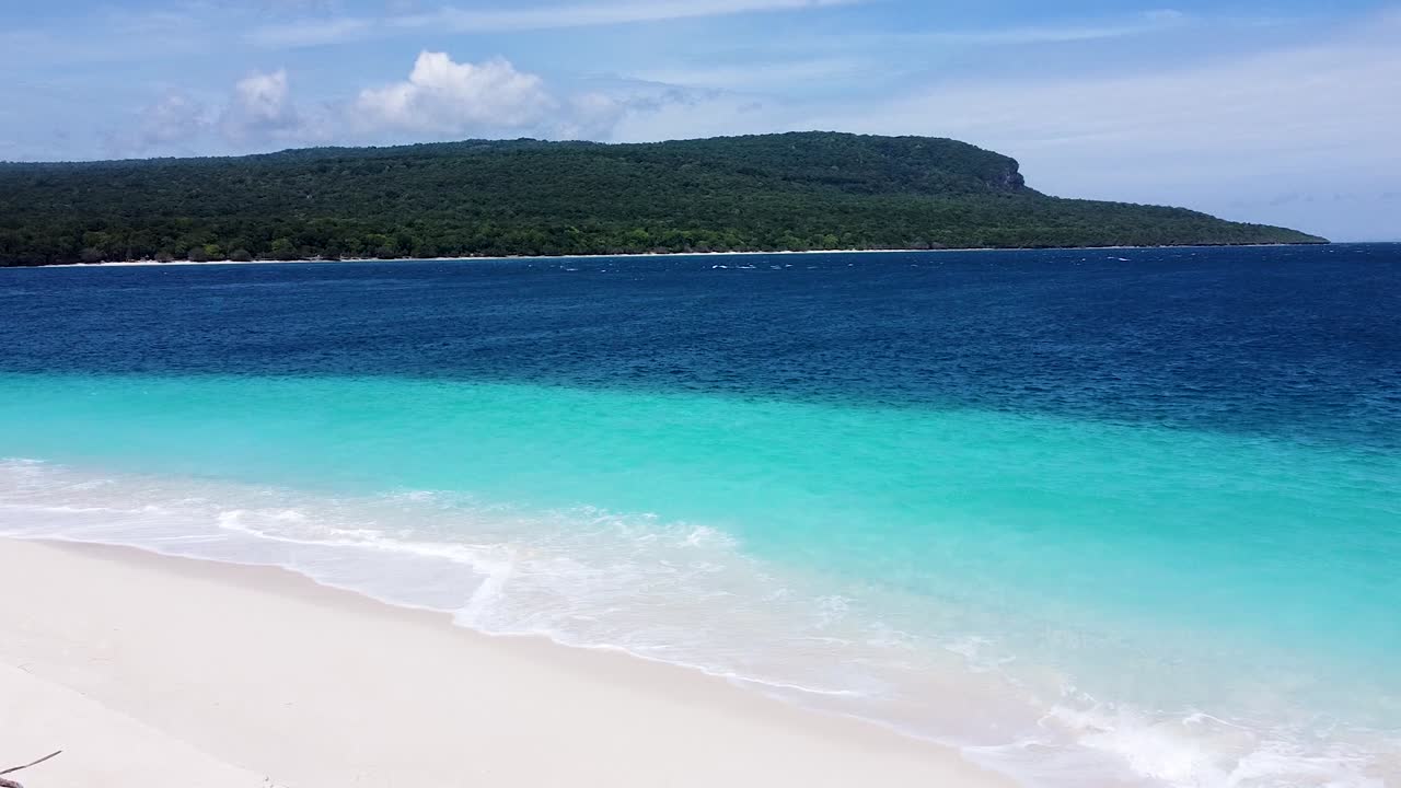 Aerial rising view over mainland of Timor-Leste covered in dense green forest trees and idyllic turquoise ocean water from Jaco Island