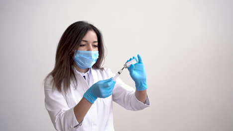 doctora con mascarilla médica llenando una jeringa con una vacuna sobre fondo blanco y espacio de copia