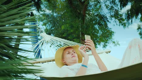 young woman resting in a hammock, using a mobile phone. connection on vacation concept