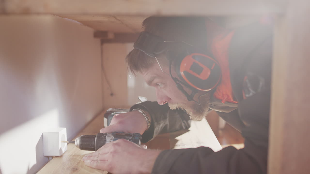 전기 기술자 는 단일 소켓 설치 를 완료 하기 위해 드릴 을 가지고 선반 아래 에 오리 를 넣는다