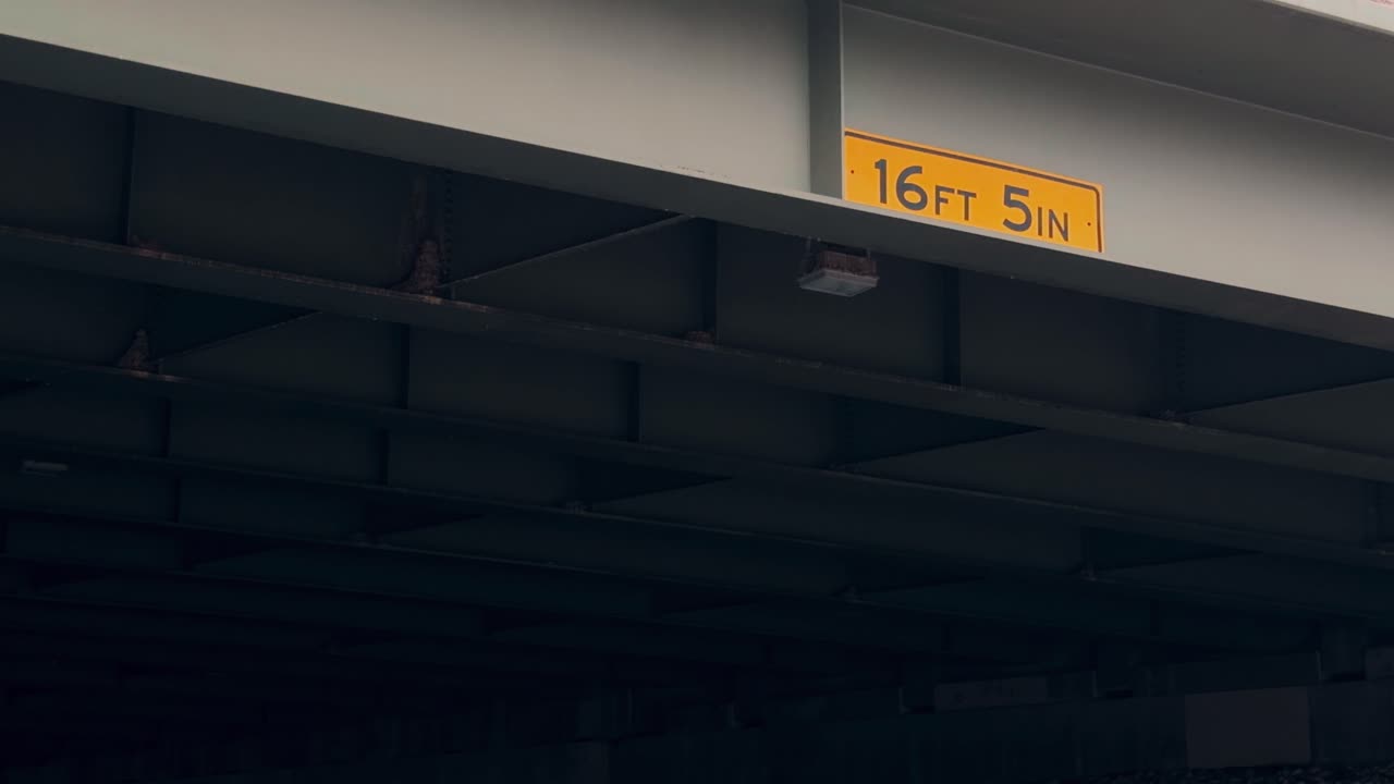 Barrido lento y constante bajo un paso elevado urbano que muestra una señal de advertencia de altura libre