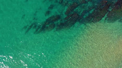fotografía aérea en un soleado día de verano del tranquilo mar turquesa en la zona costera que muestra la arena naranja y las rocas marrón bajo las aguas cristalinas de la costa de cantabria en españa