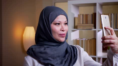 fotografía en primer plano de una empleada musulmana adulta en hijab tomando selfies en el teléfono en el lugar de trabajo en el interior de la oficina