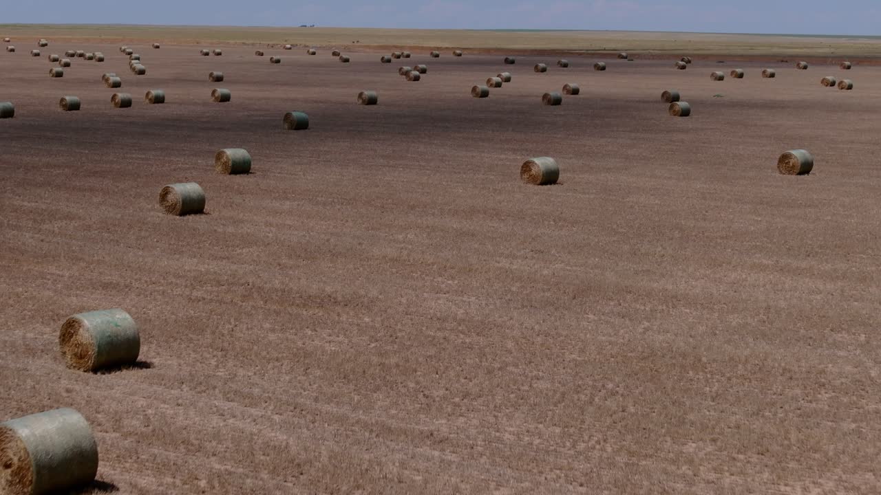Low sweeping drone pullback across empty farmland with sparse hay bales and cloud shadow textures