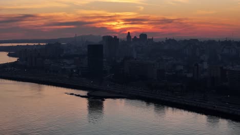 a warm sunset bathes montevideo in golden light, outlining the iconic palacio salvo and cerro against the sky, while the sun’s reflection dances softly on the río de la plata
