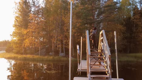 boy standing on wooden bridge enjoying golden lake sunset and orange autumn colors, in ostrobothnia, finland