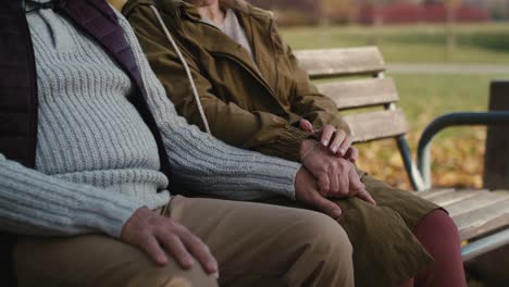 Caucasian-senior-couple-sitting-at-the-bench-at-park-and-holding-hands