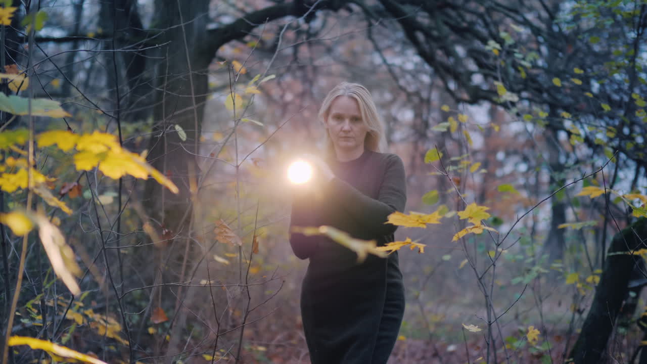 겁에 질린 여자는 황혼에 숲을 걷고 손전등으로 그녀의 길을 밝힙니다.
