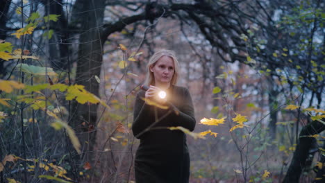 Frightened-Woman-Walks-Through-The-Woods-At-Dusk-Illuminates-Her-Way-With-A-Flashlight