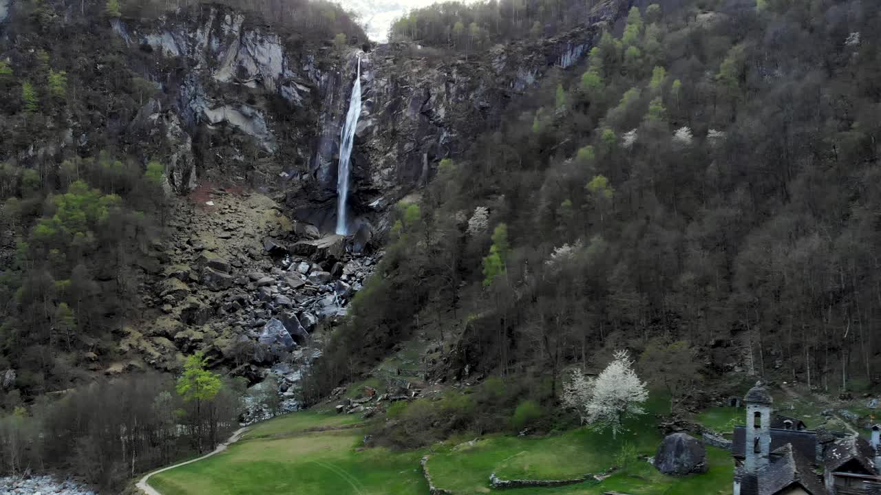 Aerial flyover with a side of the old stone house of Foroglio village in Ticino, Switzerland underneath the waterfall at dusk