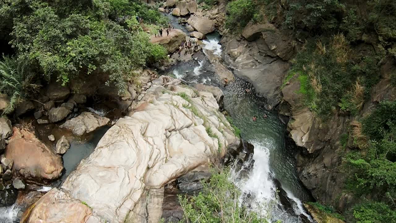 toma en cámara lenta de cascada rocosa profunda, turistas disfrutando de la brisa del agua valle abajo, sri lanka